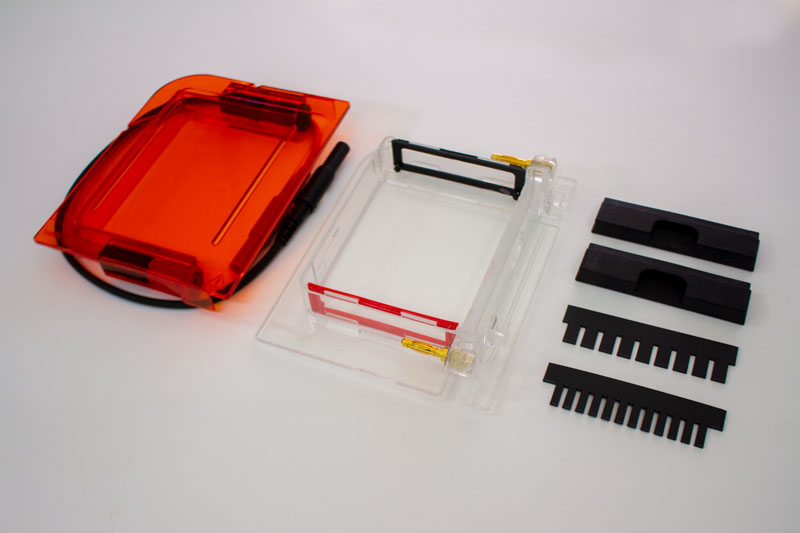 Bento Lab Gel Electrophoresis Box - all parts laid out: Orange filter acrylic lid, clear acrylic tank with red and blue electrodes, two shutters, a 9 well and a 12 well comb.